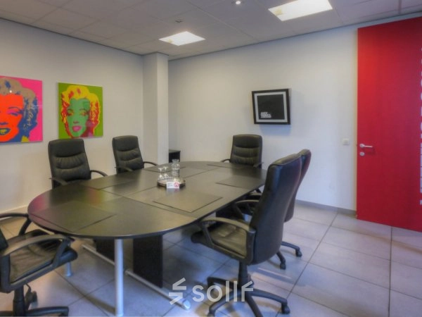 Vergaderruimte met ronde tafel en zes stoelen, kleurrijke kunst aan de muur. Kantoorruimte te huur op Middelmolenlaan 175 in Antwerpen Merksem.