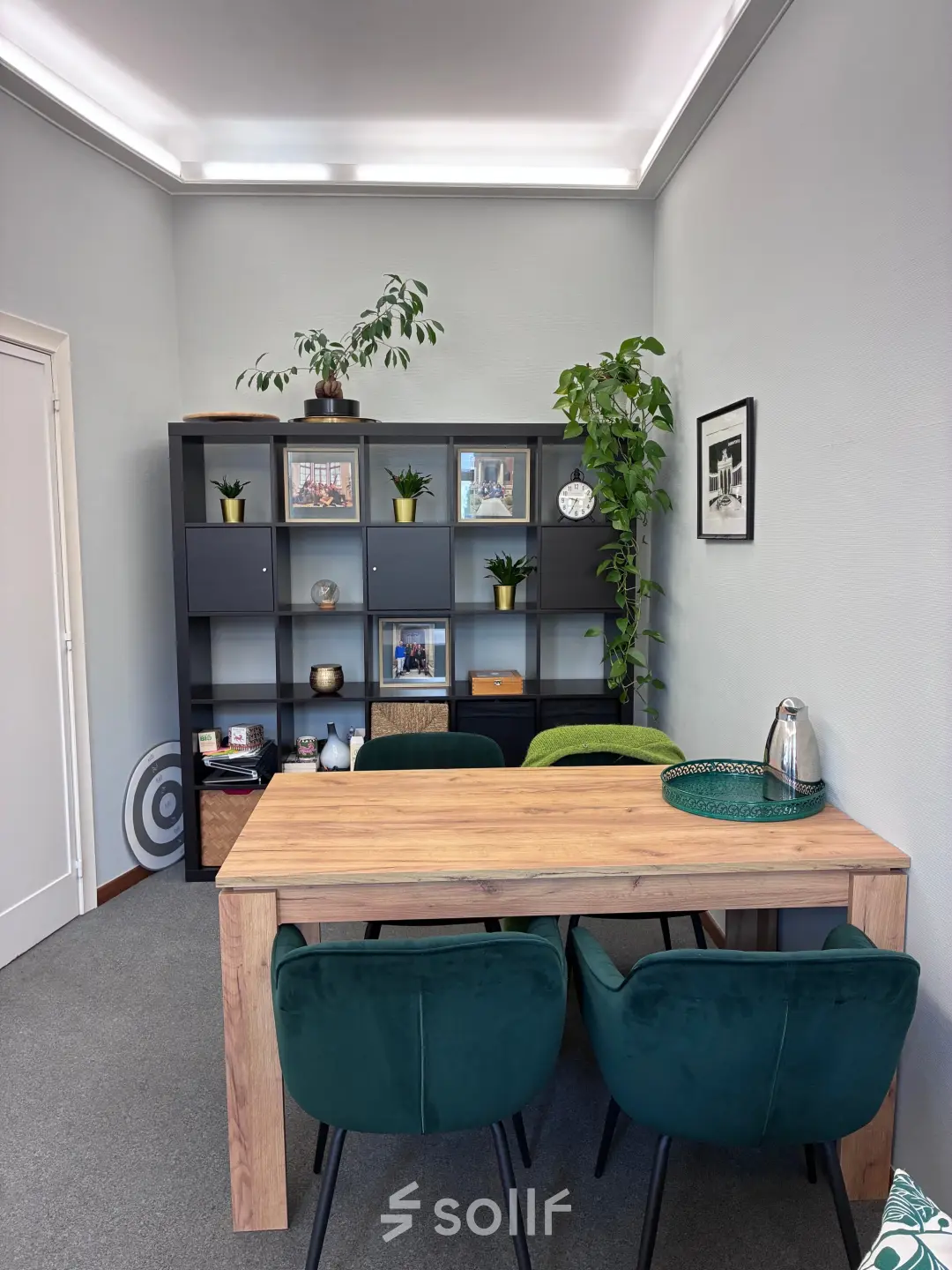 Stijlvol gemeubileerde kantoorruimte te huur op Avenue Palmerston 3 in de Europese Wijk van Brussel, met een houten tafel en groene stoelen, omringd door planten en wanddecoratie.