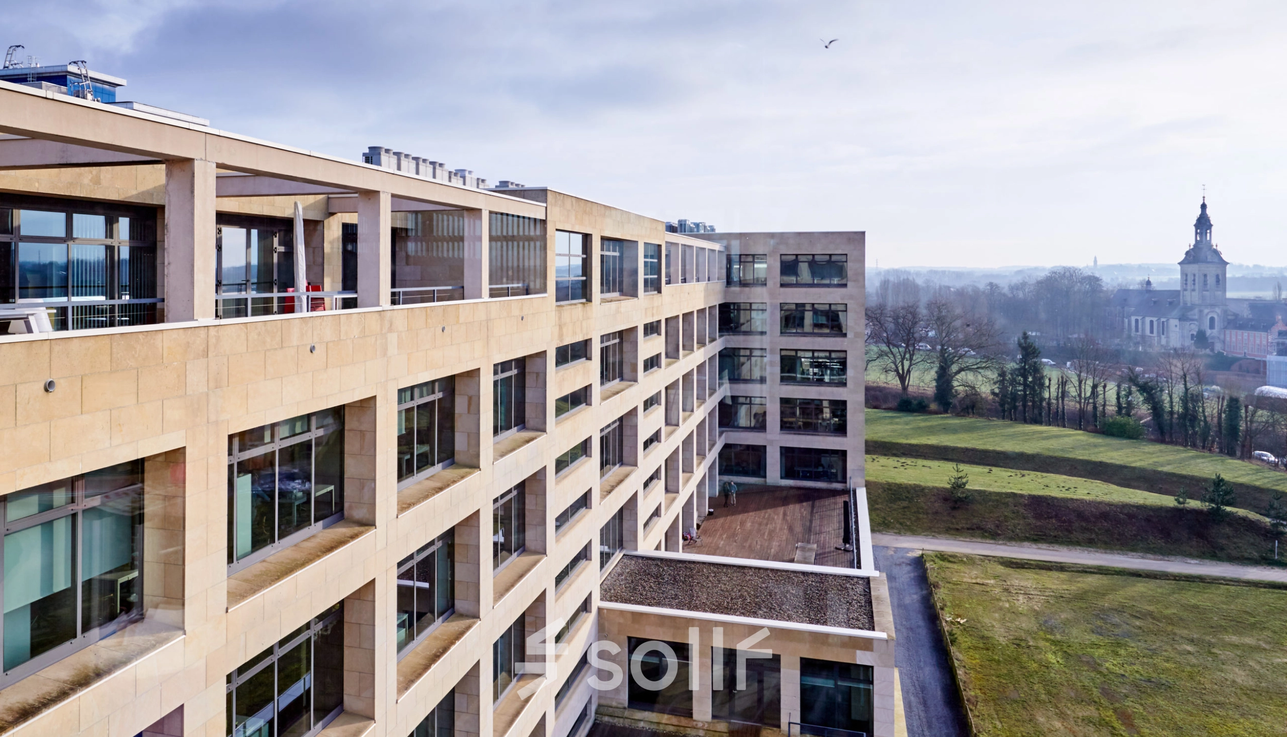 Buitenzijde van een groot kantoor te huur op Philipssite 5 in Leuven met moderne architectuur en veel ramen omgeven door groen.