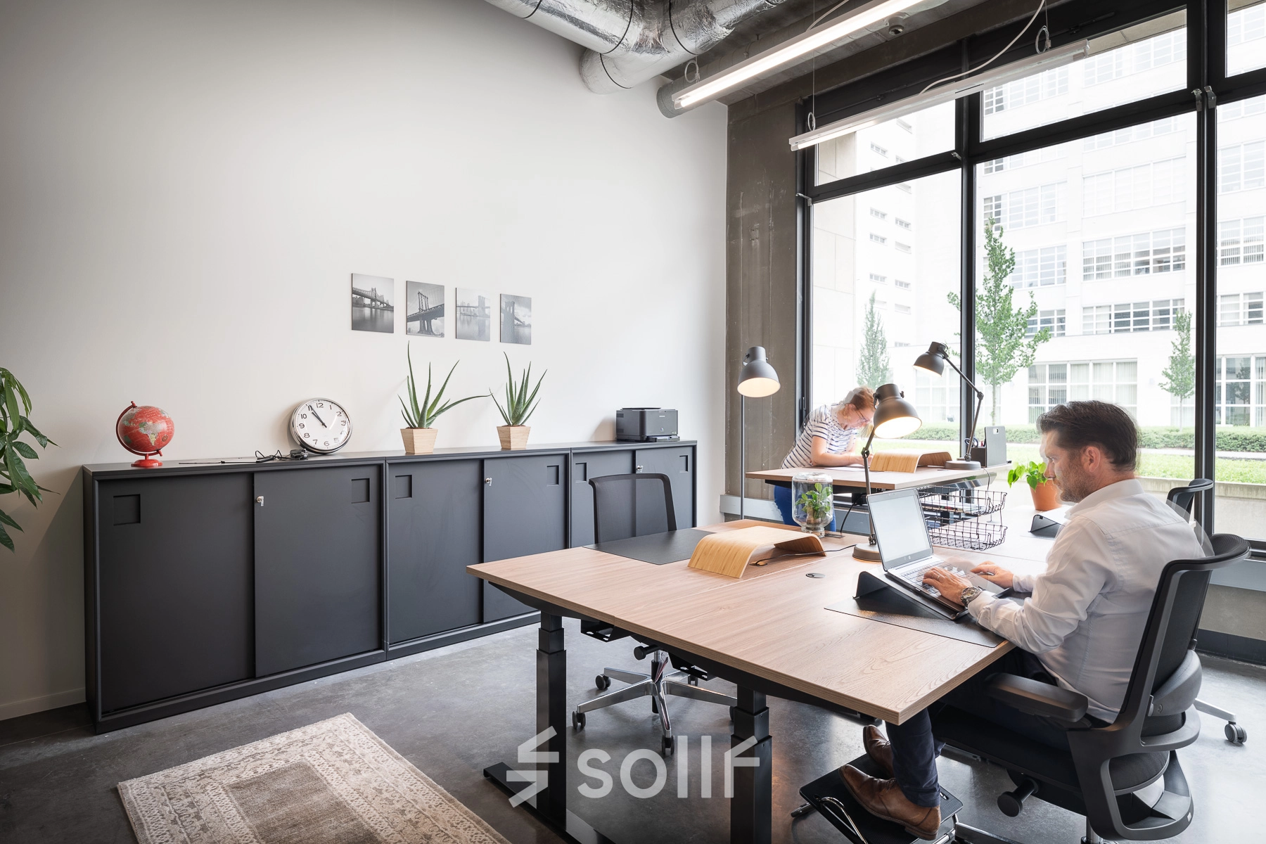 Moderne kantoorruimte te huur in Leuven op Philipssite 5, met strakke meubels en grote ramen die veel licht binnenlaten. Mensen zijn aan het werk, bezig op hun laptops. Ideaal voor wie een kantoorruimte wil huren.