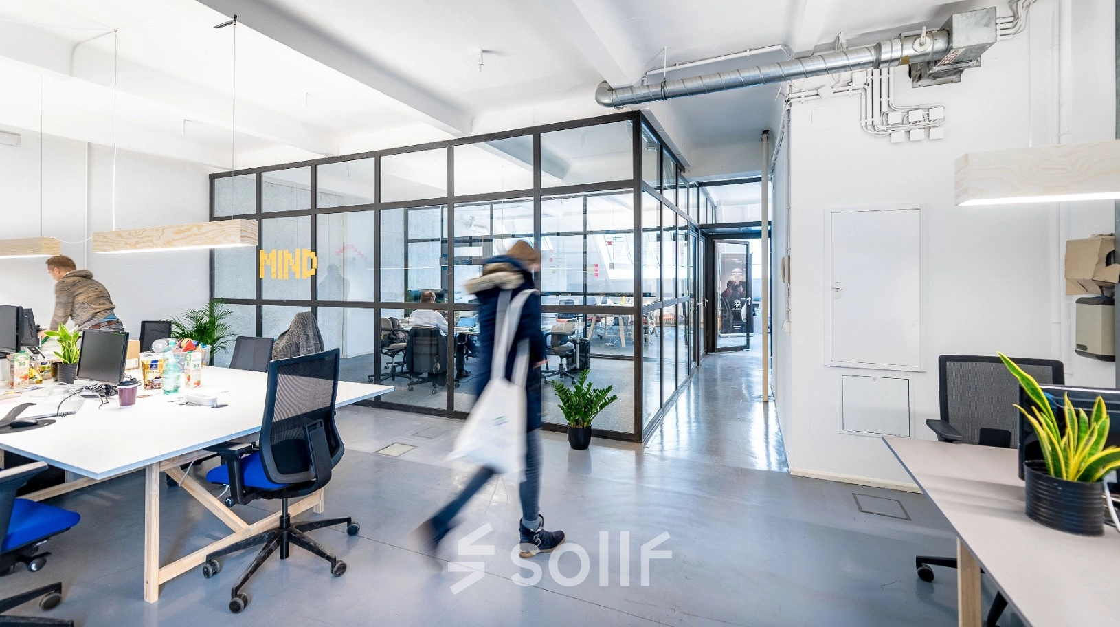 Modernes Büro in Berlin Kreuzberg mit offenen Arbeitsbereichen, Schreibtischen und Glaswänden. Personen arbeiten oder bewegen sich durch den Raum.
