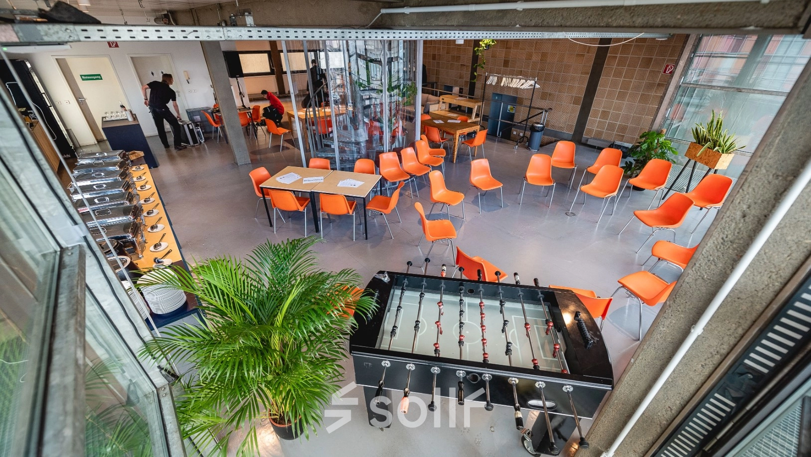 Büroraum in der Rudi-Dutschke-Straße 23, Berlin Kreuzberg, mit orangenen Stühlen, Tischfußballtisch und Pflanzen. Ideal für kreatives Arbeiten und Meetings.