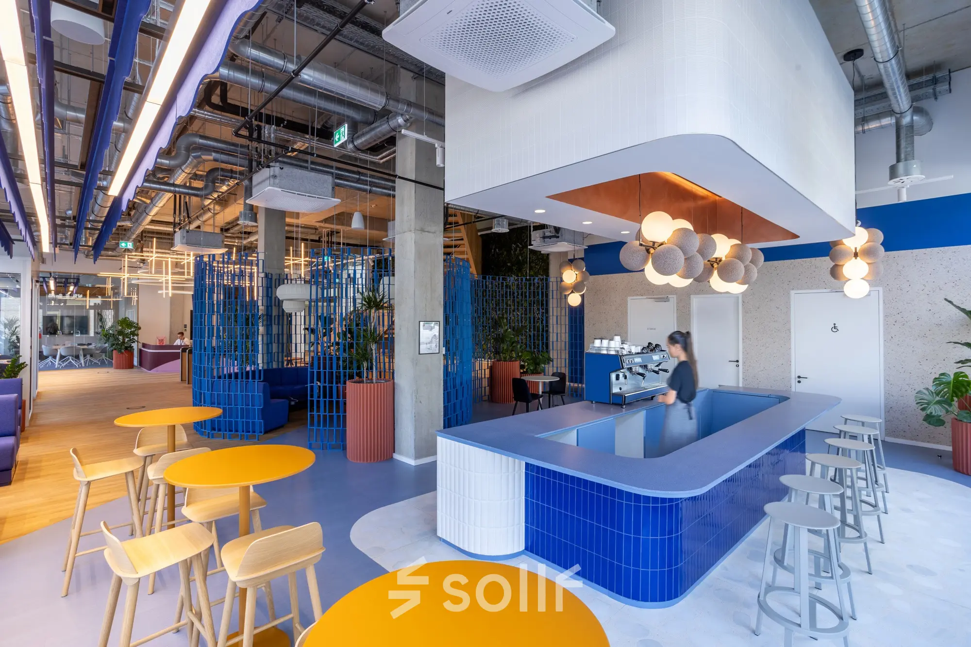 Modernes, offenes Büro in Berlin Mitte mit einer stilvollen Café-Bar, farbenfrohen Möbeln und einladender Atmosphäre. Perfekt zum Büro mieten oder für kreative Arbeitsbereiche geeignet.