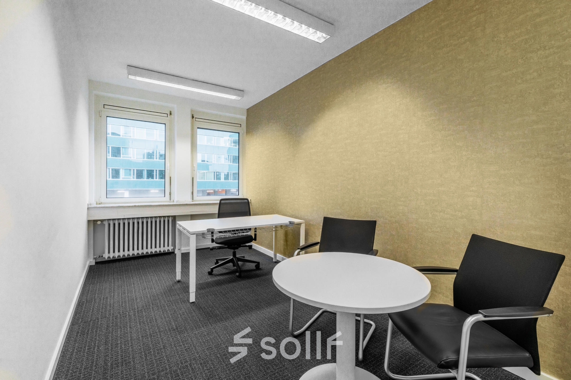 Helles Büro mit zwei schwarzen Stühlen, einem runden Tisch und einem Schreibtisch mit Bürostuhl. Geeignet zum Bürofläche mieten im Düsseldorfer Altstadtviertel.
