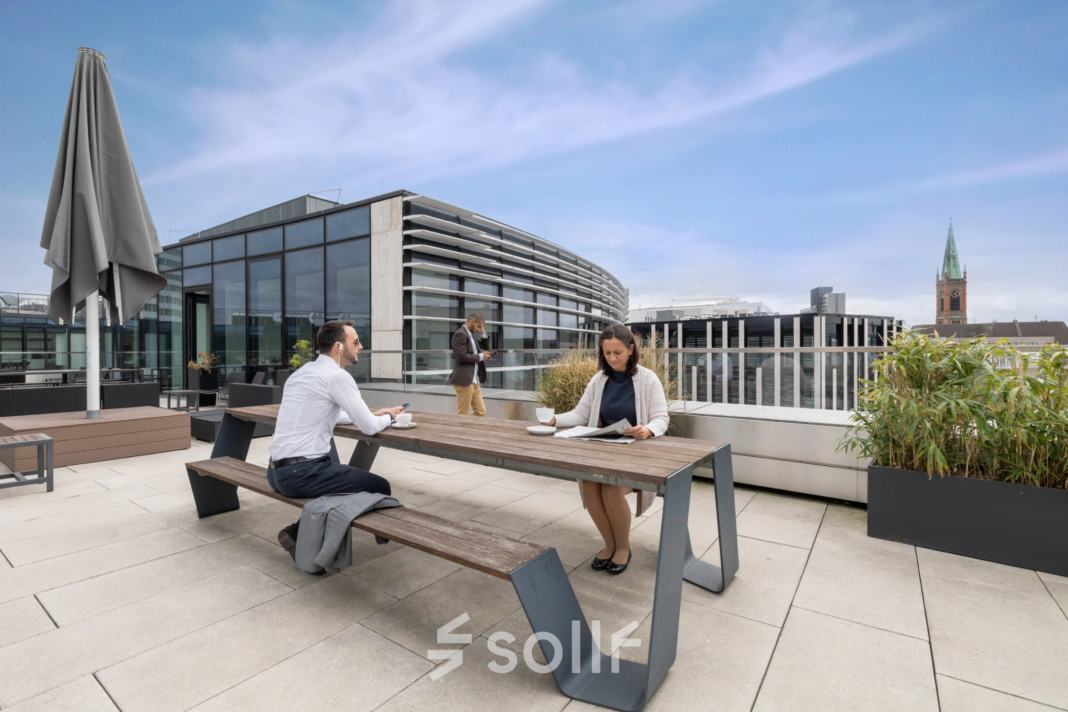 Moderne Büroterrasse an der Königsallee 2b in Düsseldorf Altstadt mit zwei Personen, die an einem Tisch arbeiten und eine dritte Person, die telefoniert.