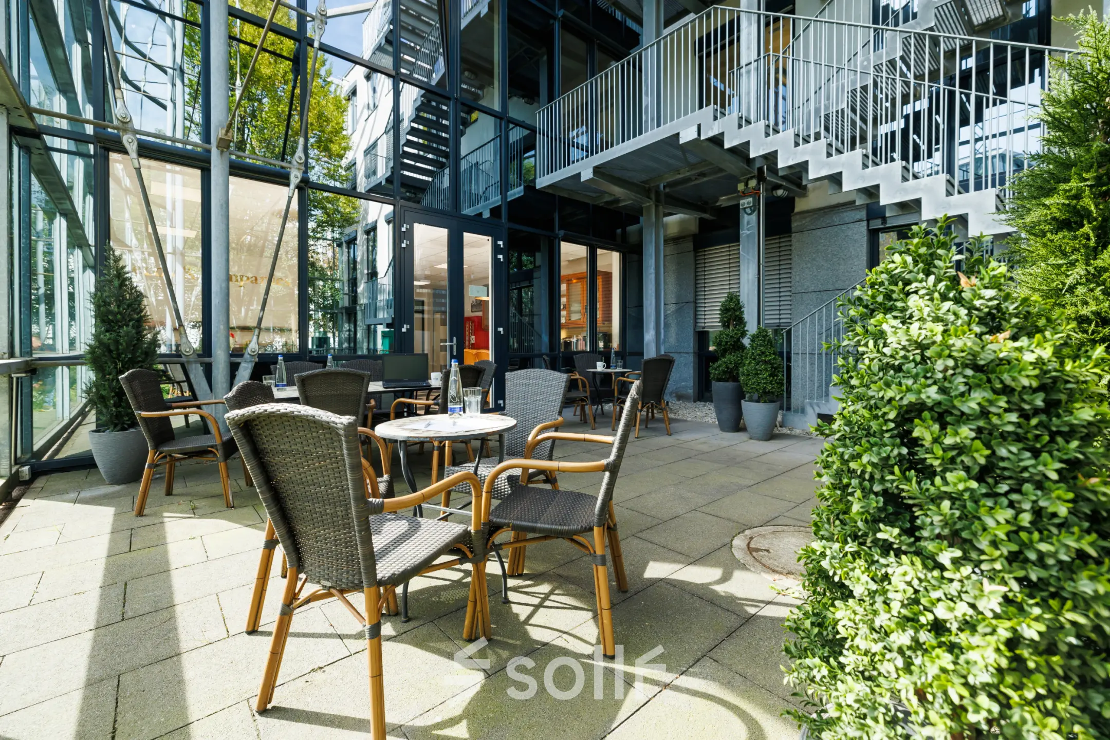 Moderner, heller Eingangsbereich mit Glastüren und Außenbestuhlung in München Laim. Ideal, um ein Büro zu mieten an der Landsberger Straße 155.