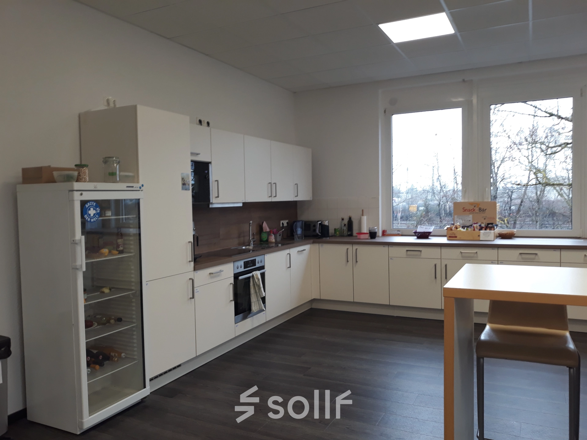 Helle Büroküche zur Miete in München Pasing mit Kühlschrank, Ofen und zwei Barhockern; ideal für Meetings oder Pausen.