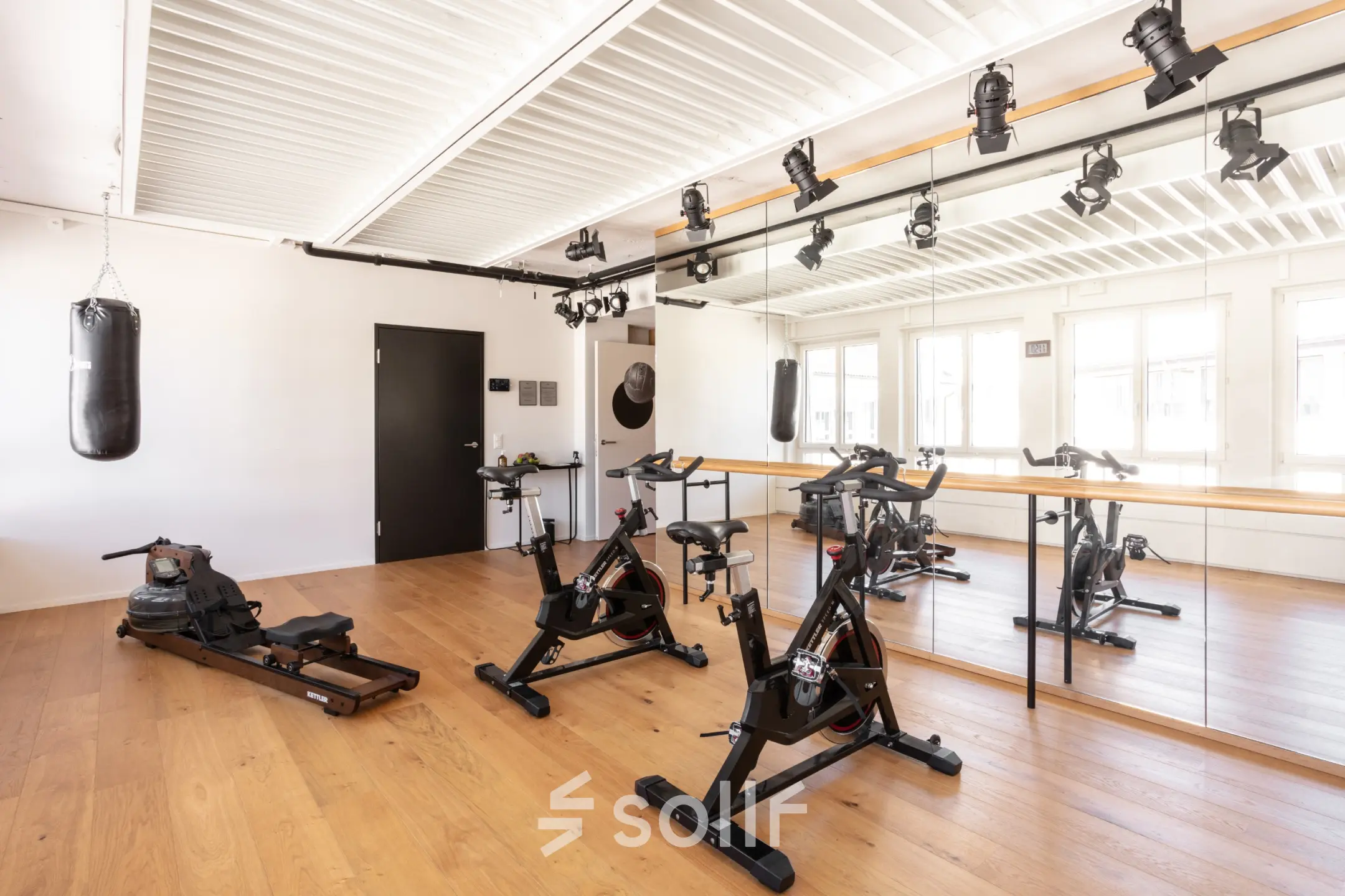 Helle Bürofläche in Zürich City mit Fitnessgeräten, Spiegelwand und Lichtelementen an der Decke. Ideal für kreative Mietlösungen. Perfekt für Unternehmen, die ein außergewöhnliches Büro mieten möchten.