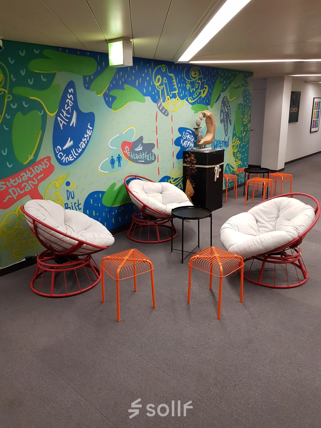 Bunter Loungebereich im Büro am Mythenquai 26, Zürich Enge, mit modernen Sesseln und Hockern vor einer kunstvoll bemalten Wand. Ideal zum Büroraum mieten.