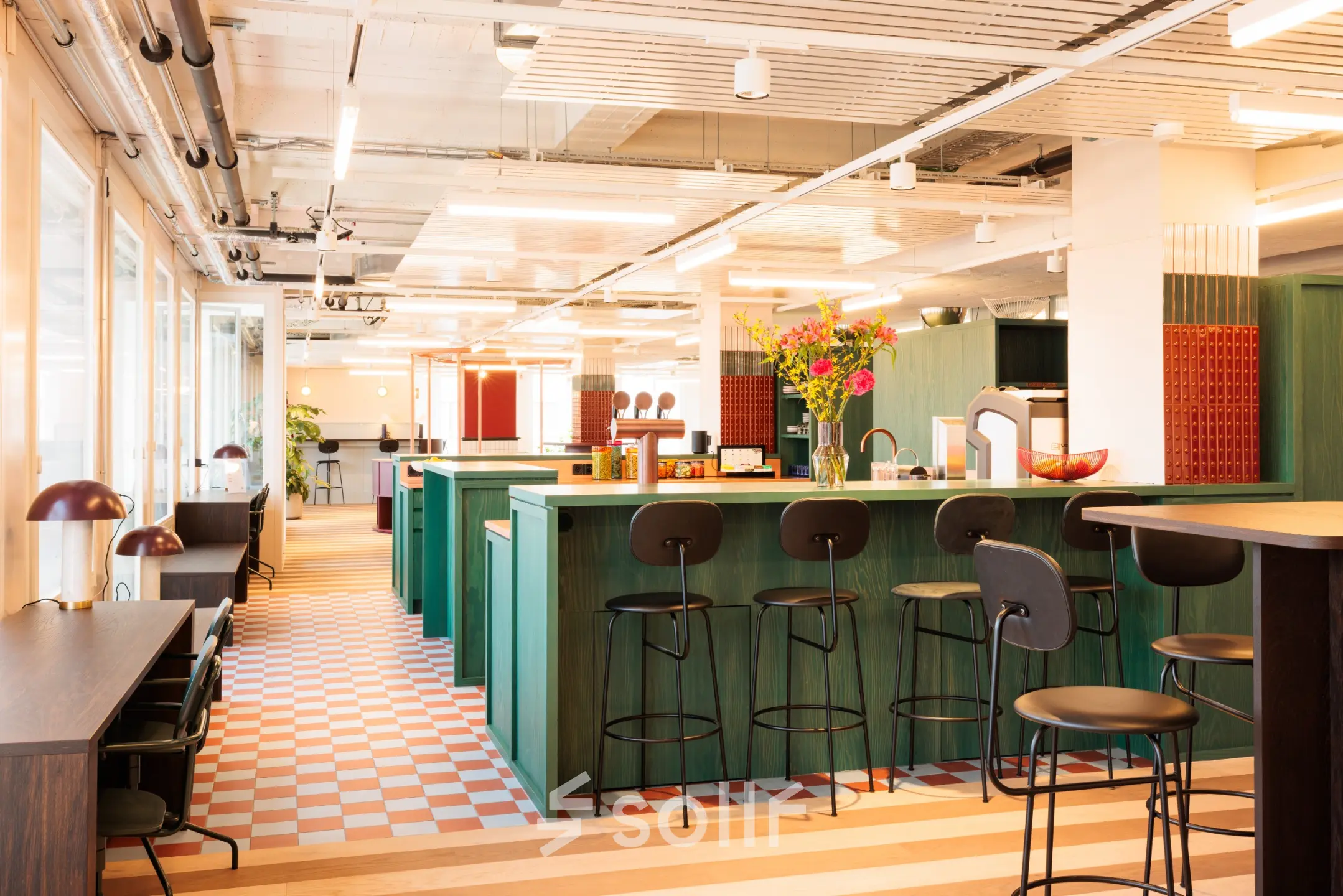 Ein farbenfrohes, modernes Büro mit offenen Arbeitsbereichen und hohen Hockern an einer Theke in Zürich Enge. Perfekt für alle, die Bürofläche mieten möchten.