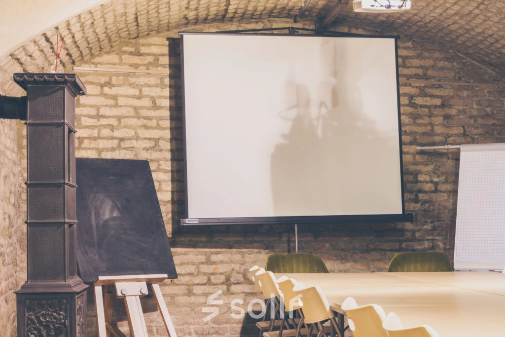 Interior of a furnished office space at Zimmermanngasse 8, 1090 Vienna, featuring a long table with chairs, a projector screen, and a flip chart, ideal for office space rental.