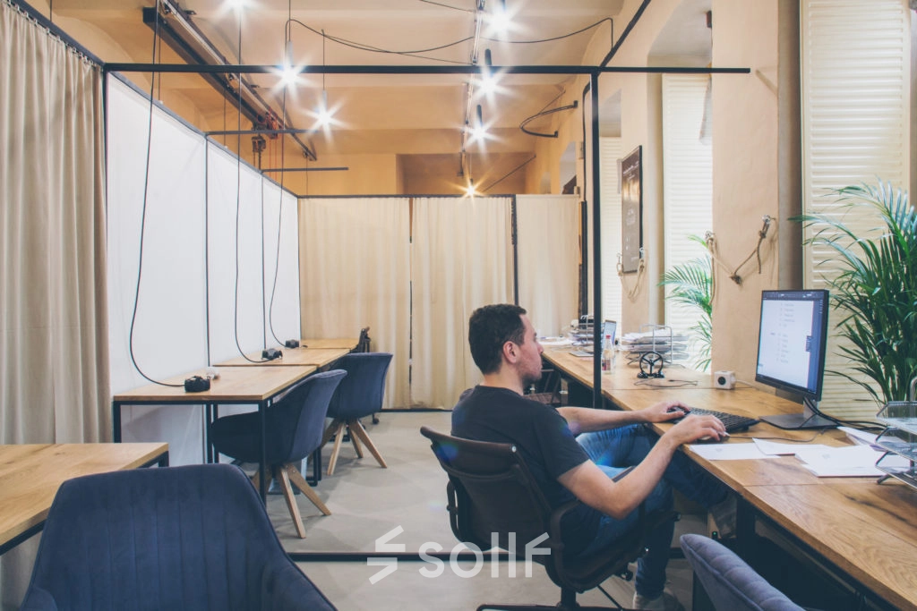Spacious office to rent in Vienna's Alsergrund district at Zimmermanngasse 8. A person is working at a computer in a modern, open-plan workspace with wooden desks and comfortable seating.