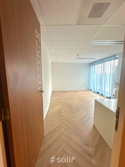 Interior view of an office space at Hollandse Kade 38, Abcoude, ideal for office space rental, featuring wooden flooring, white walls, and large windows with blue curtains.