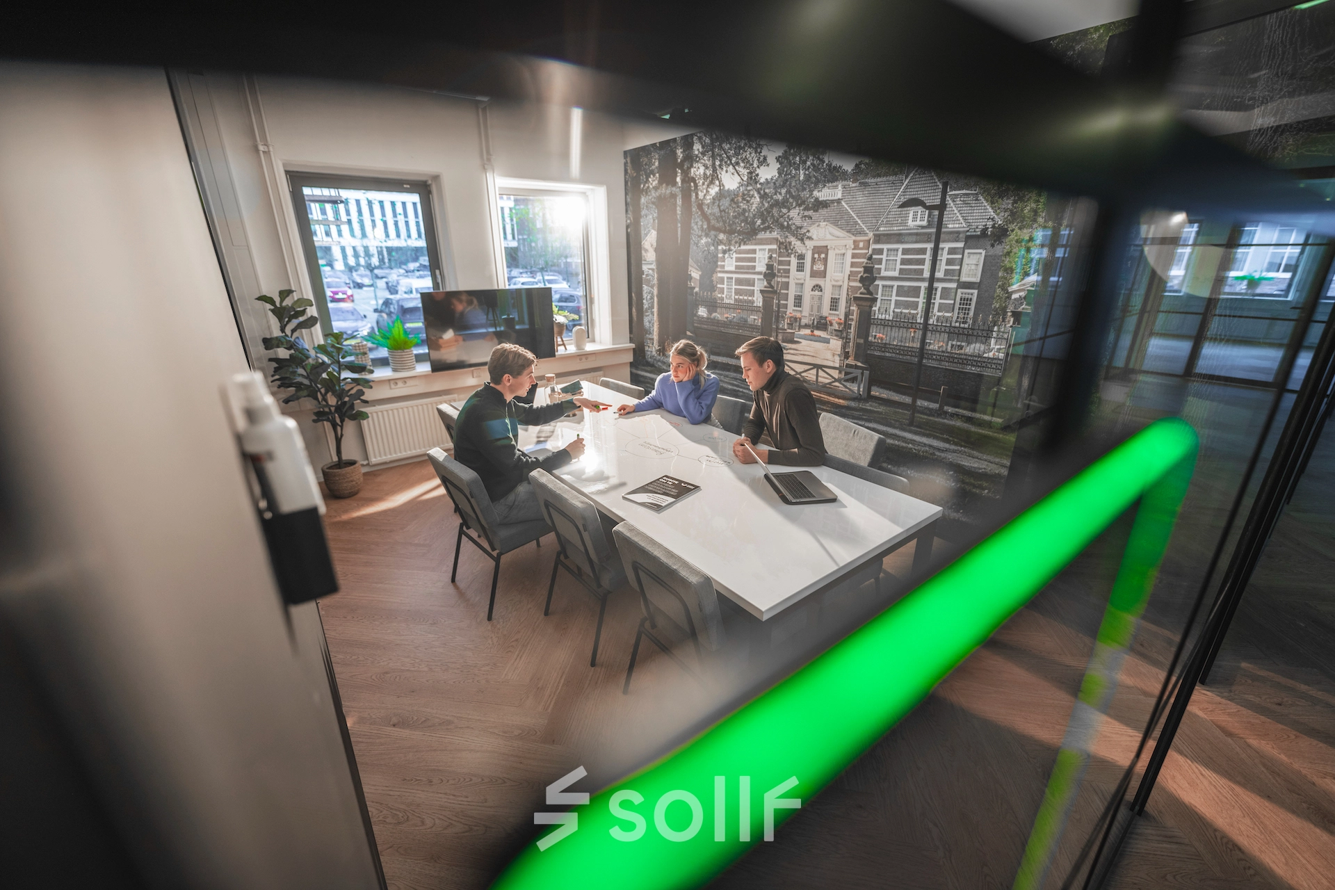 Modern office space featuring a large table with three people engaged in a business meeting, equipped with tablets and documents. Bright, professional setting ideal for office space rental.