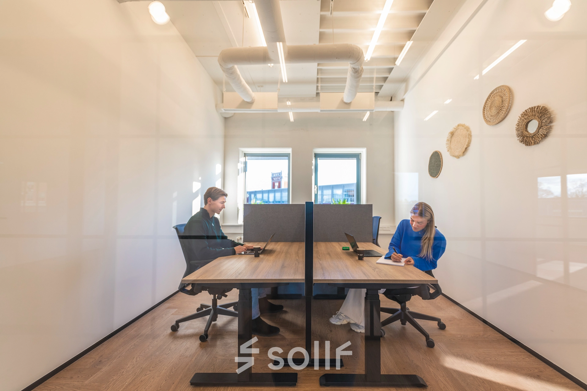 Bright office space in Almelo at Egbert Gorterstraat 2-14 featuring two people working at desks, ideal for office space rental. Modern design with large windows and stylish décor, providing a productive environment.