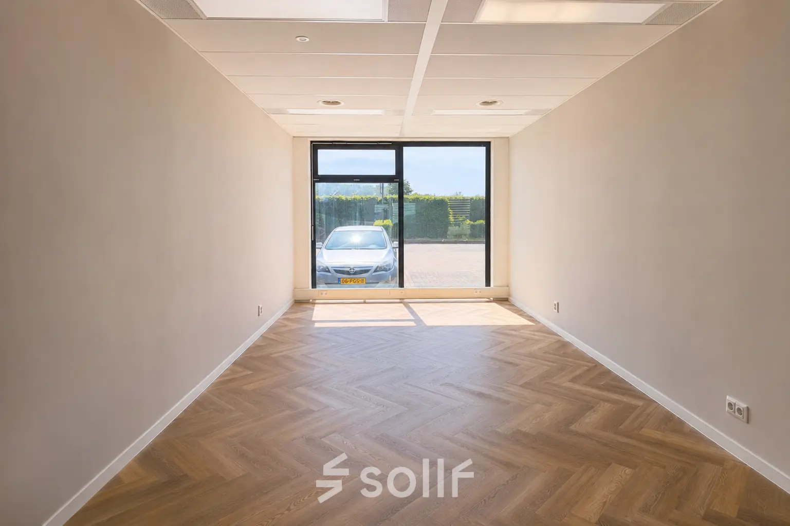 Unfurnished office space available for rent at Veluwezoom 15, Almere Stad, featuring natural light and wooden flooring with a view of the parking area.