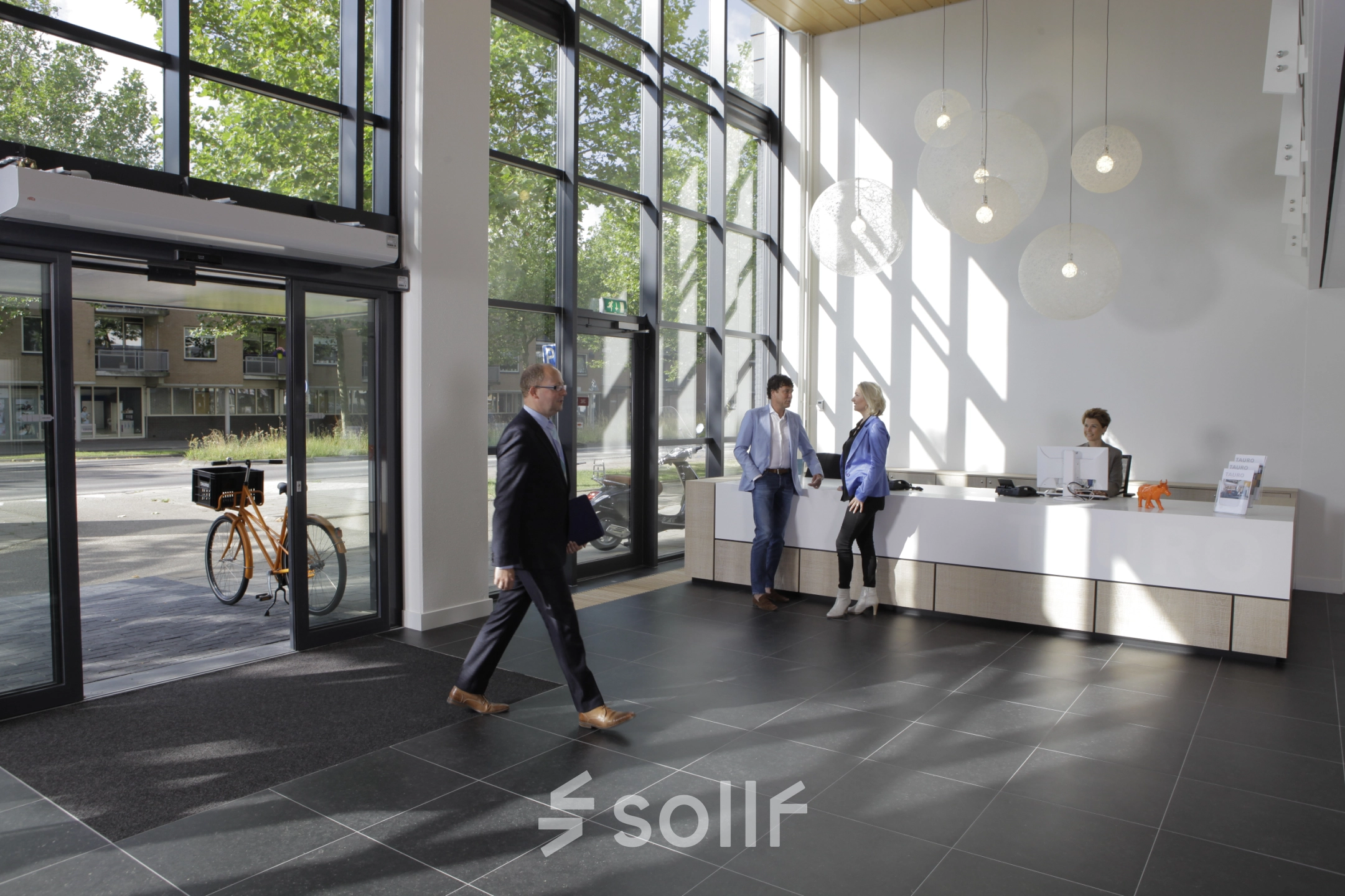 Spacious office reception area at Europalaan 16, Alphen aan den Rijn, with people discussing rental options and a receptionist assisting inquiries. Perfect for those looking to rent office space.