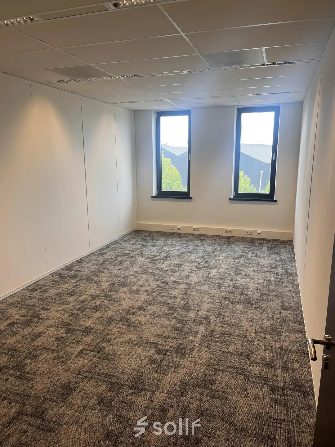 Empty office space with carpet flooring and two windows at Leidse Schouw 2 for rent in Alphen aan den Rijn.