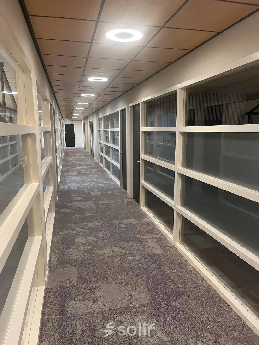 Long hallway with carpeted floor and glass partition walls in an office space for rent at Leidse Schouw 2, Alphen aan den Rijn.