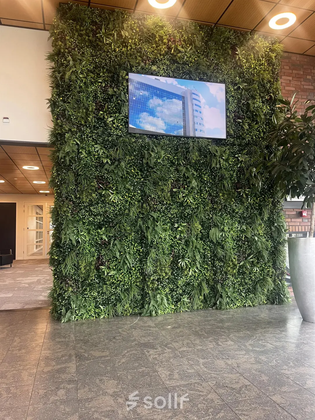 Bright lobby at Leidse Schouw 2, Alphen aan den Rijn with a lush green wall and TV screen, ideal for office space rental.