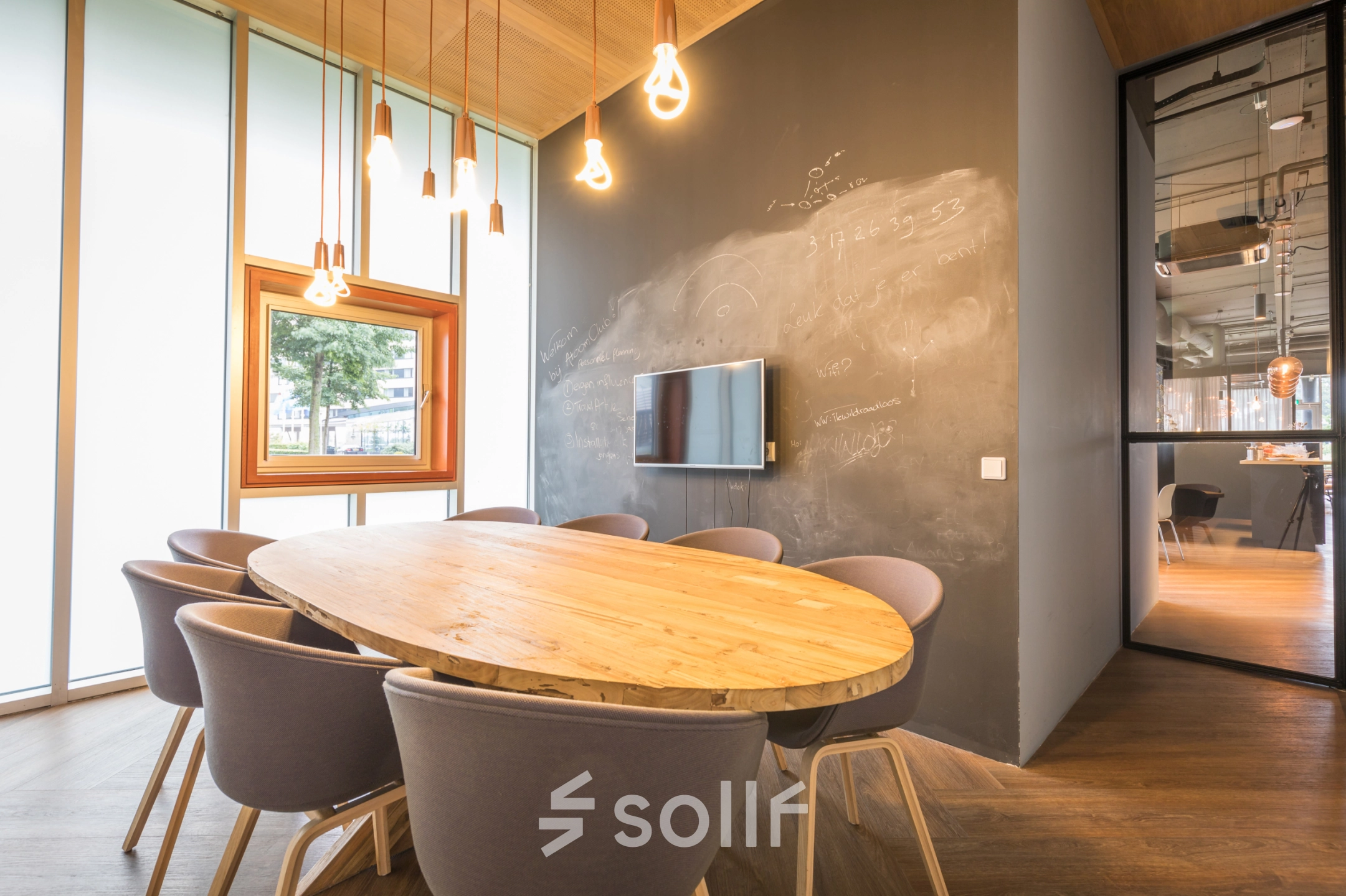 Modern conference room at Maanlander 47, Amersfoort Calveen, suitable for office space rental, featuring a wooden table, chairs, chalkboard wall, and pendant lights.
