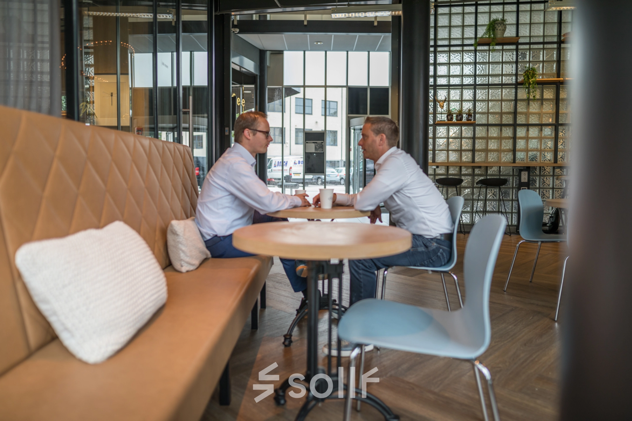 Two people having a business discussion in a stylish furnished office to rent at Maanlander 47, Amersfoort Calveen, featuring modern decor ideal for office space rental.