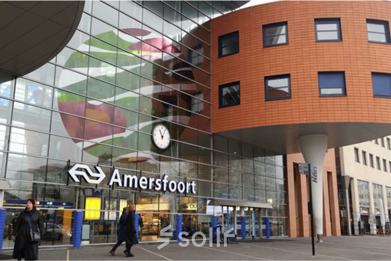 Exterior view of Amersfoort Centraal Station with modern design elements and people walking by.