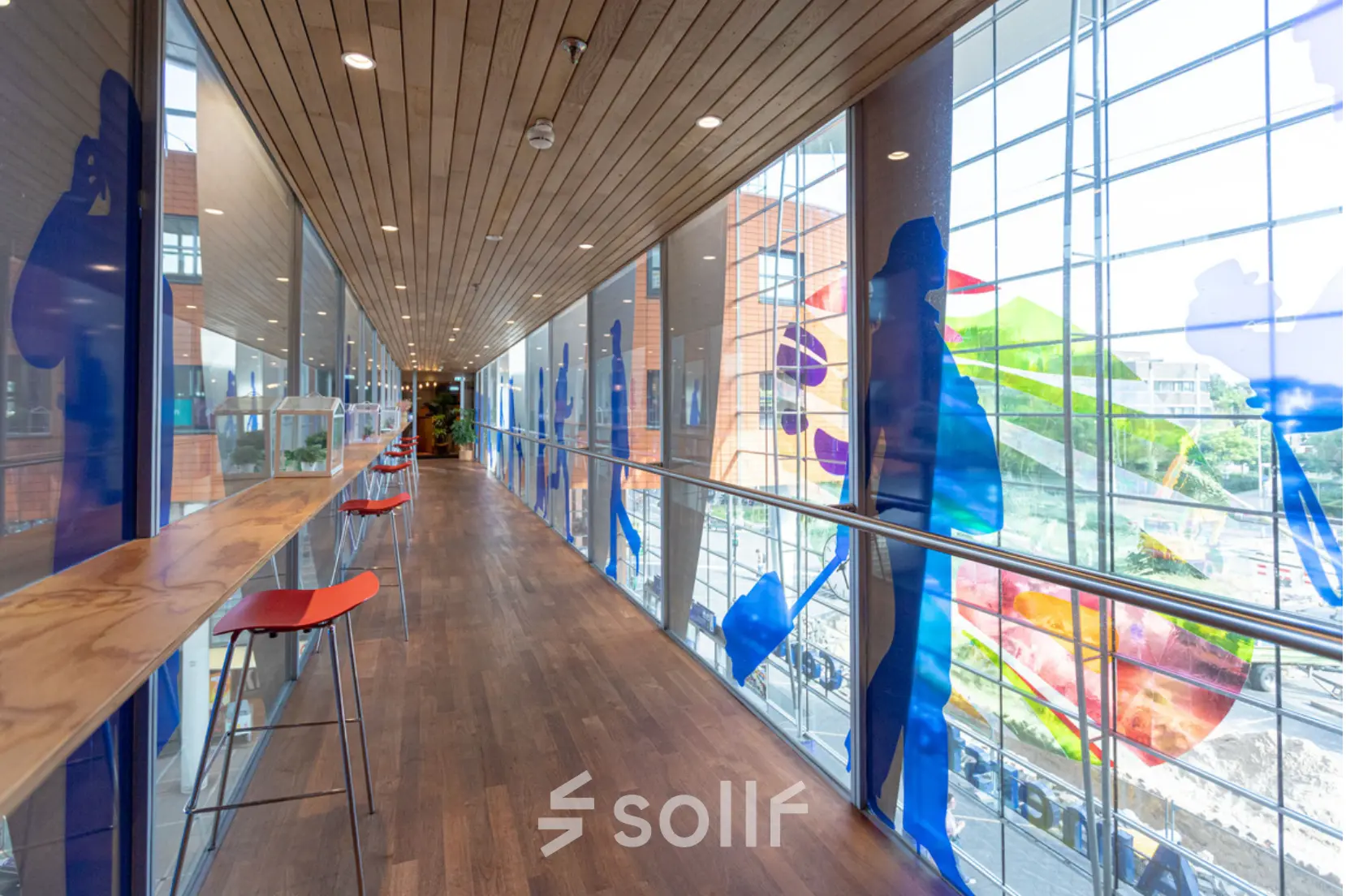 Bright corridor with high windows and colorful artwork at Amersfoort Centraal Station, ideal for break time in your rented office space.