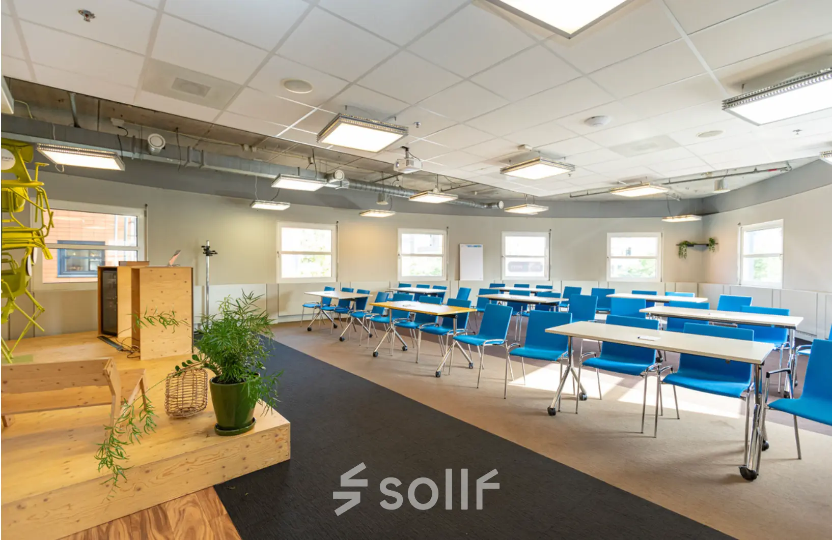 Bright and functional office space available for rent at Stationsplein 49, Amersfoort Centraal Station. Featuring rows of blue chairs and white desks, perfect for business activities.