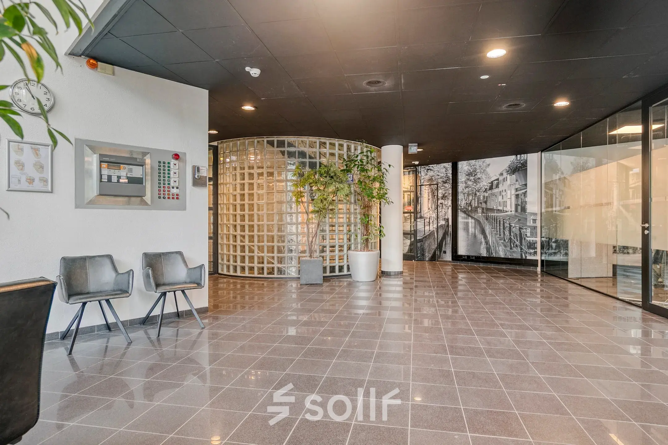 Spacious entrance area in a modern office to rent at Asch van Wijckstraat 2-4, featuring sleek tile flooring and a glass block wall for an open, professional feel.
