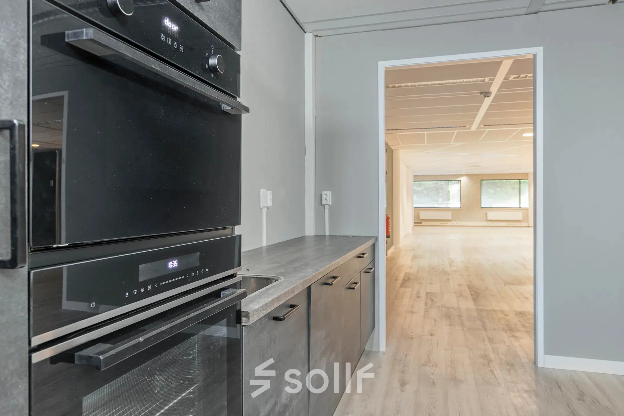 View of an office space rental in Amersfoort Centrum featuring a small kitchen area leading to an open workspace with large windows.