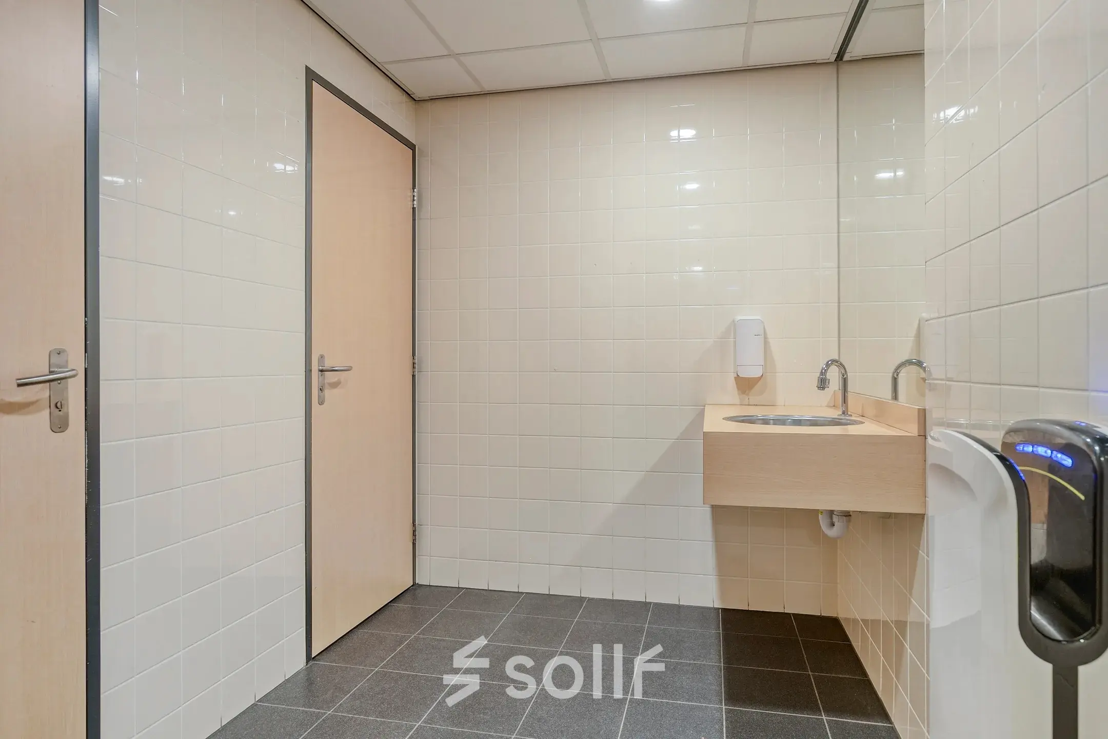 Office restroom with tiled walls, a wooden door, and a sink located at Asch van Wijckstraat 2-4 in Amersfoort Centrum, suitable for office space rental.