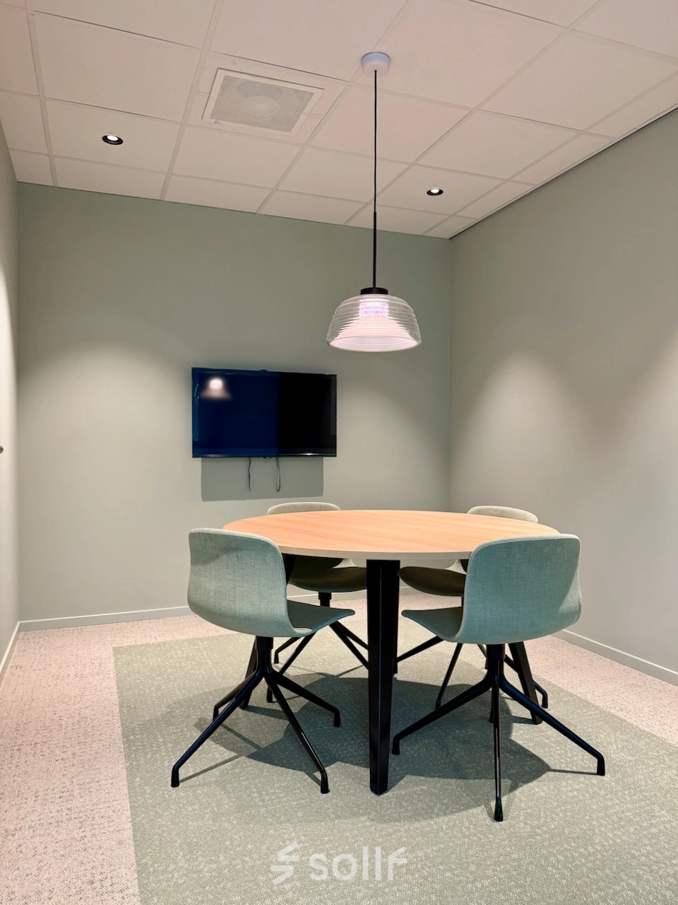 Modern office space featuring a round meeting table with stylish chairs and a wall-mounted TV, available for office space rental in Amstelveen.
