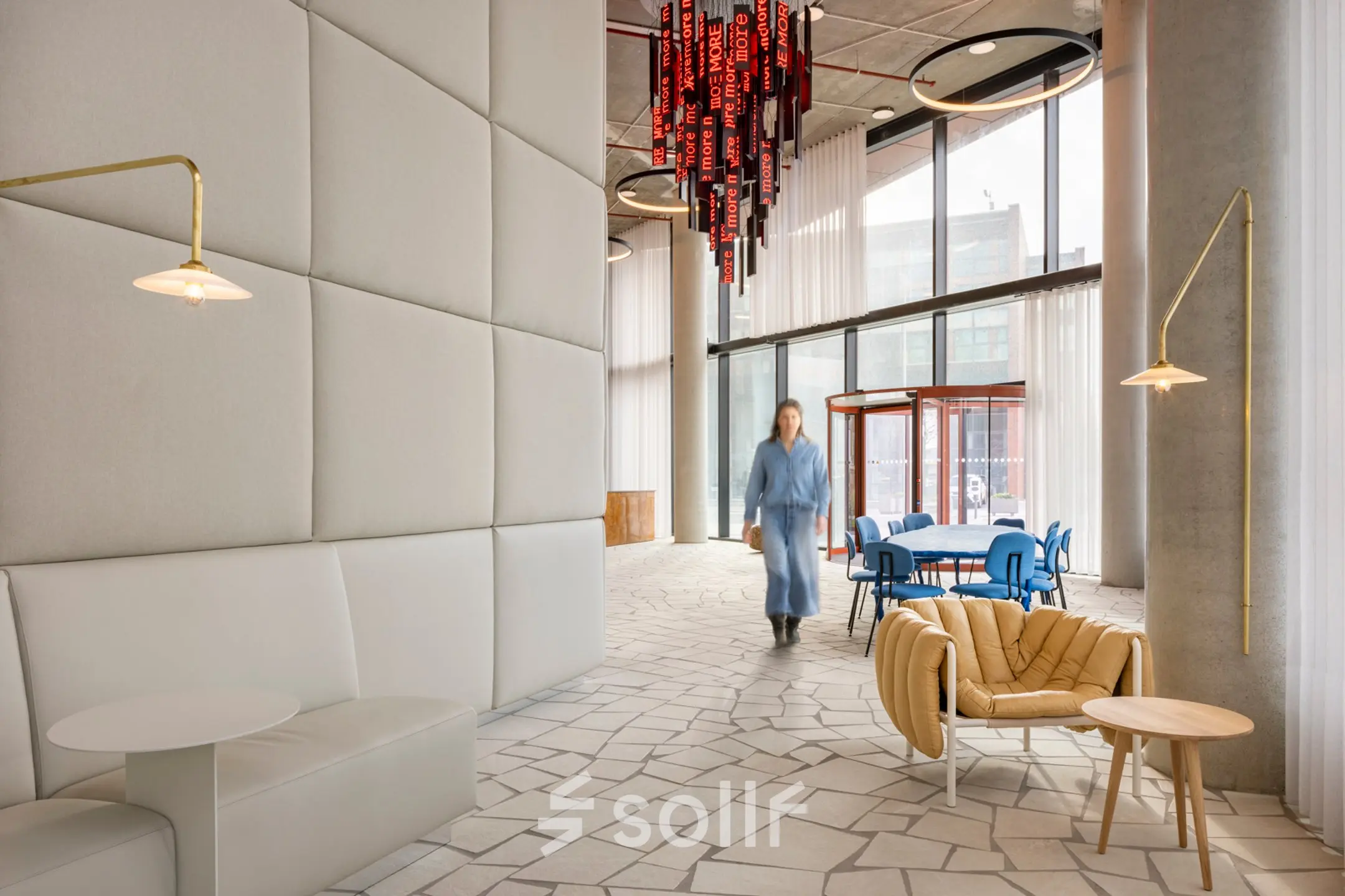 Modern interior of an office space at H.J.E. Wenckebachweg 230-258, Amsterdam Amstel Business Park, featuring contemporary seating and large windows. A person walks past, enhancing the dynamic workspace atmosphere, ideal for office space rental.