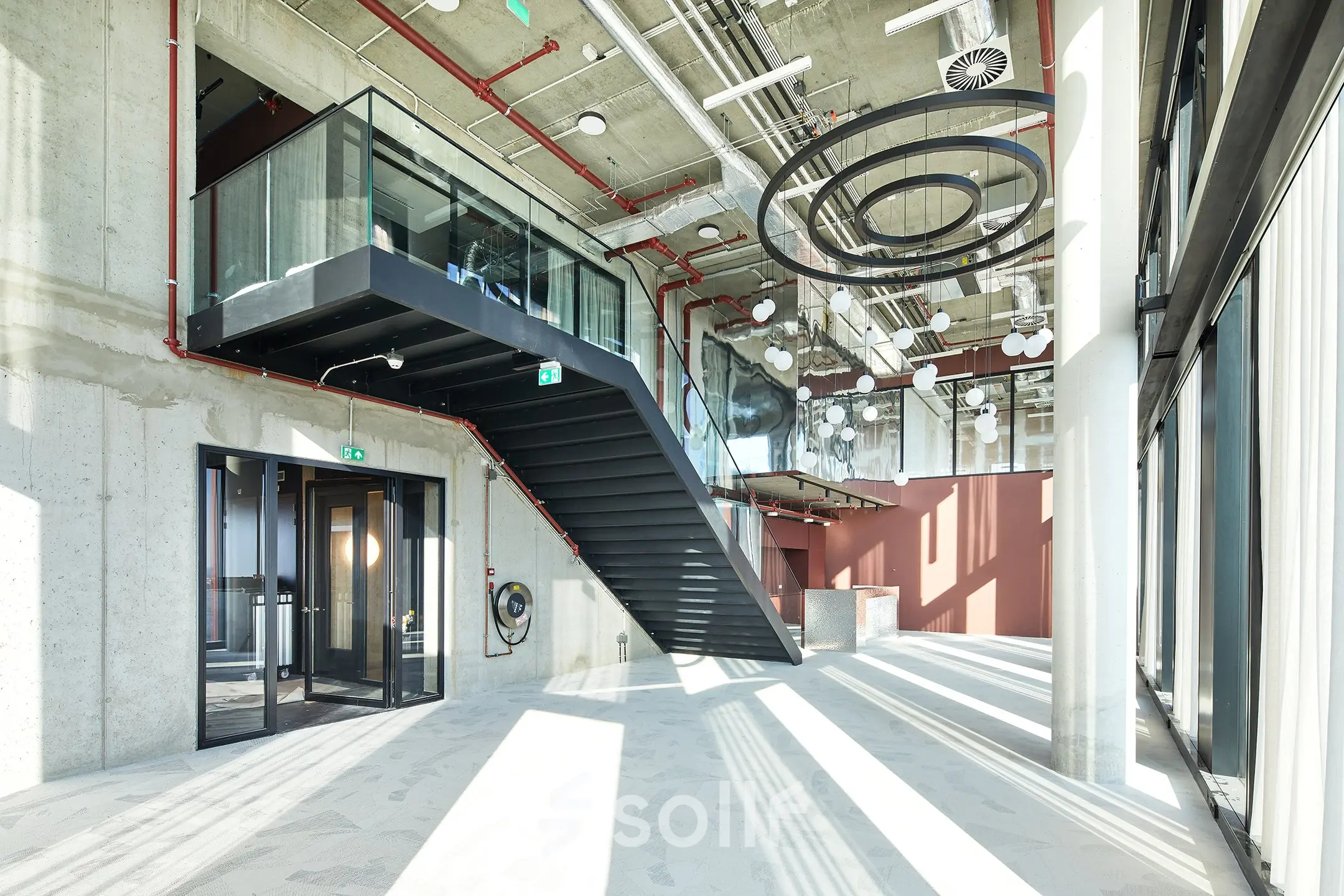 Modern office space with high ceilings and industrial design in Amsterdam Amstel Business Park, featuring large windows and a striking staircase, ideal for office space rental.