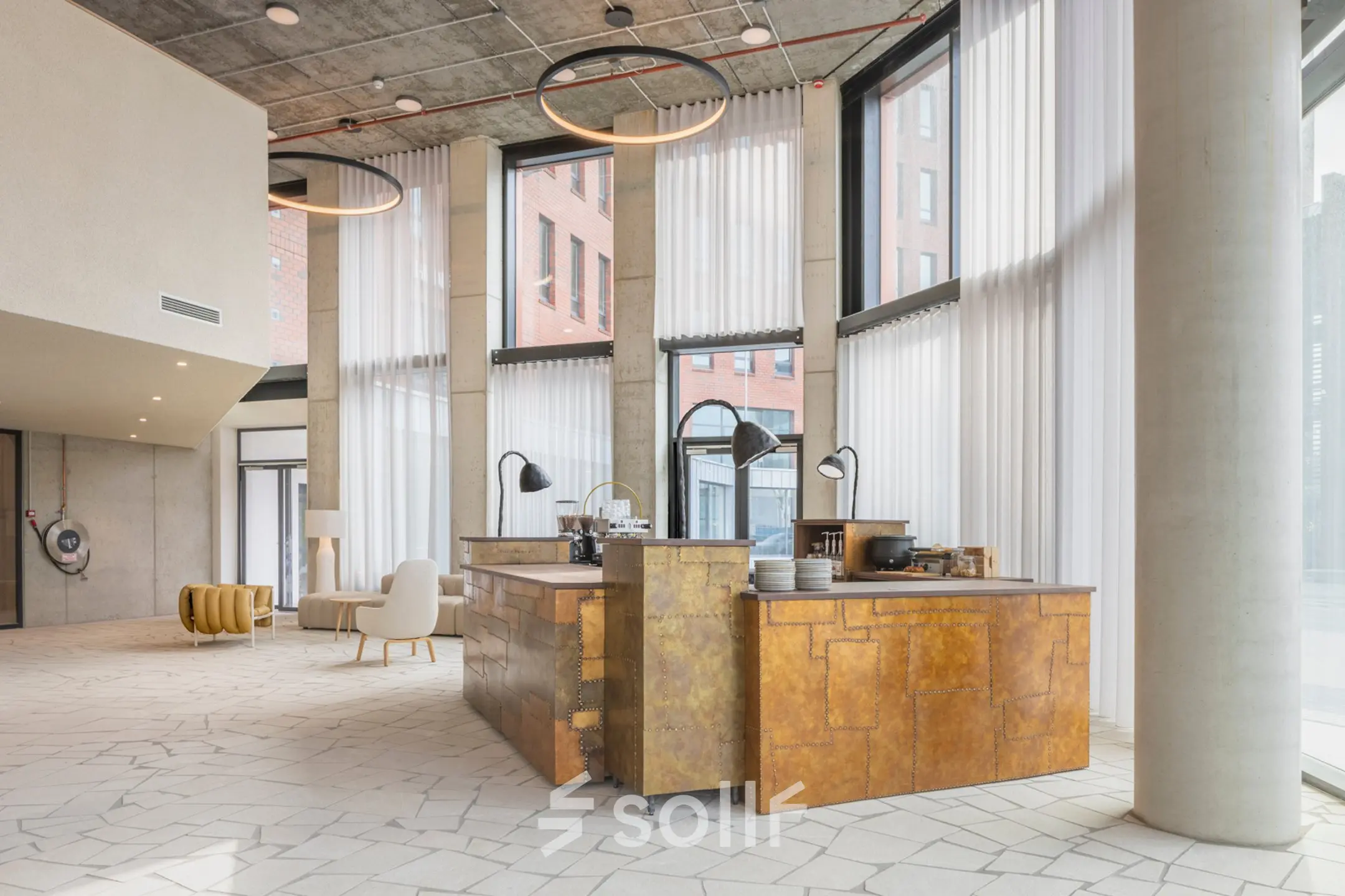 Spacious and modern interior of an office with high ceilings and large windows. Features a central seating area and a unique wood-paneled counter, available for office space rental in Amsterdam Amstel Business Park.
