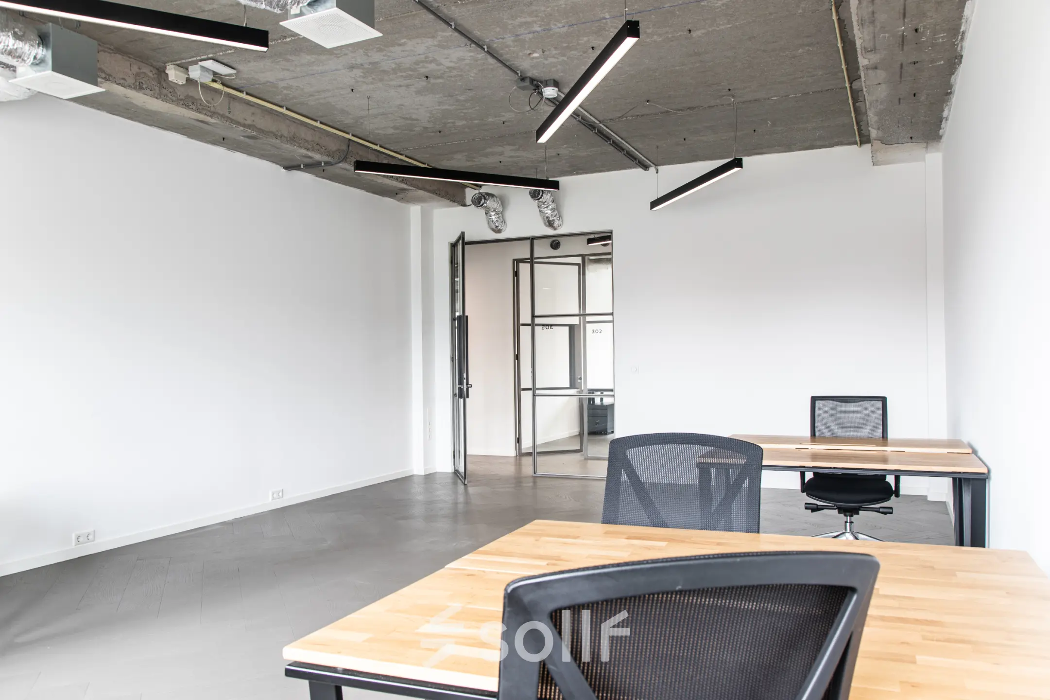 Modern office space with wooden desks and black chairs, featuring industrial-style ceiling lights at the Amsterdam Amstel Business Park.