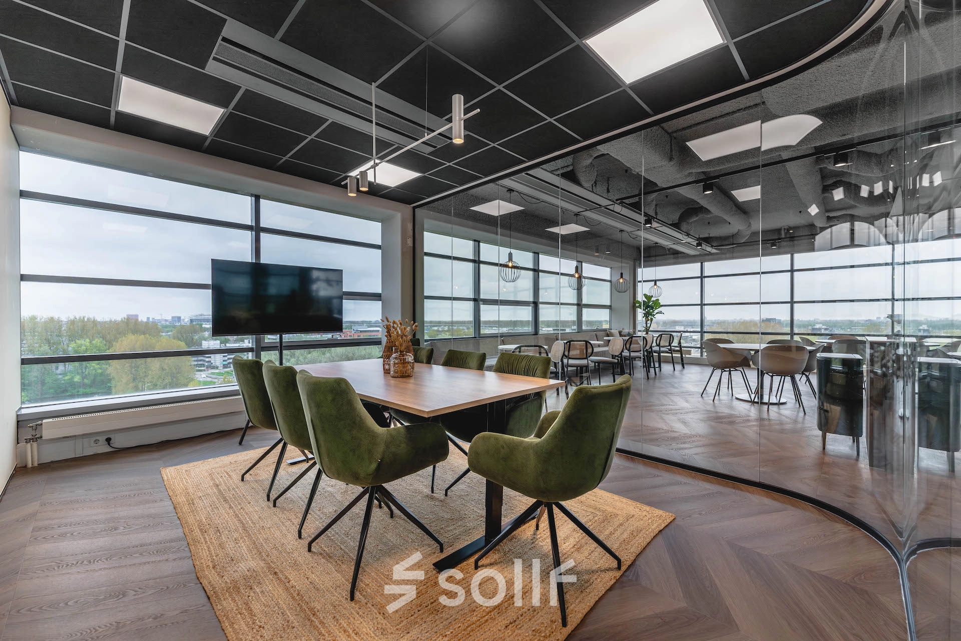 Spacious office space at Joop Geesinkweg 201 featuring large windows, green chairs, and glass partitions. Ideal for office space rental in Amsterdam Amstel Business Park.