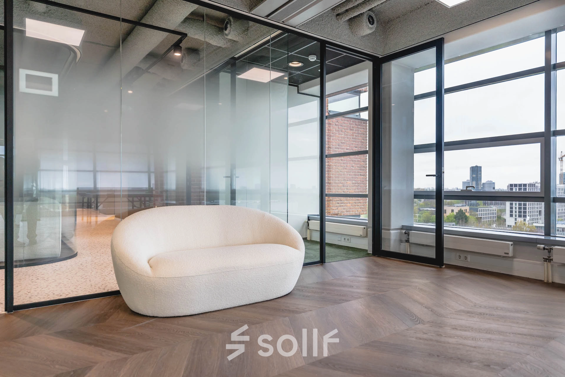 Modern office space at Joop Geesinkweg 201, featuring a sleek interior with glass walls and a stylish sofa, ideal for rent at Amsterdam Amstel Business Park.