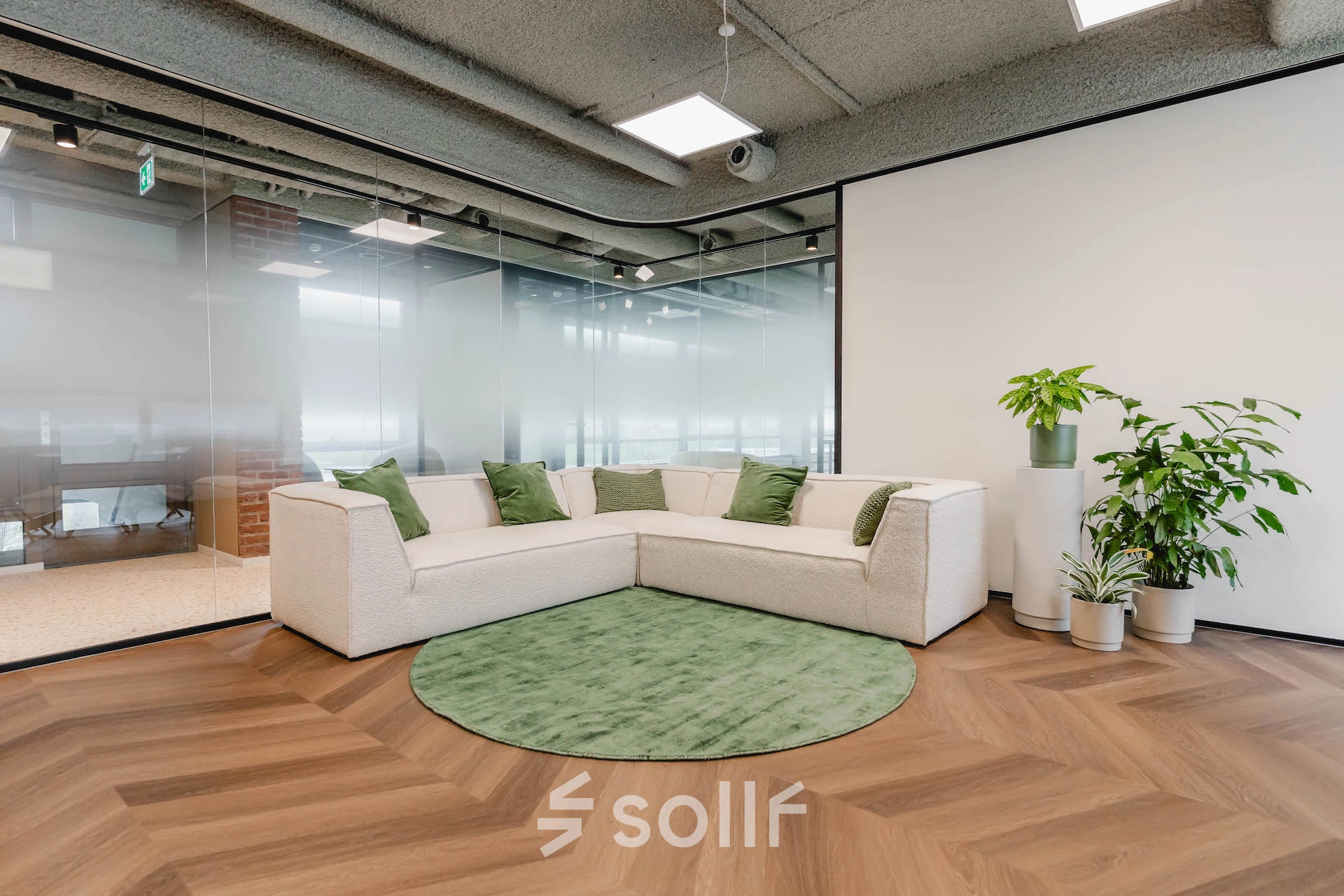 Modern office lounge with a corner sofa and greenery at Joop Geesinkweg 201, suitable for casual meetings or breaks. Consider this inviting option for office space rental in Amsterdam Amstel Business Park.