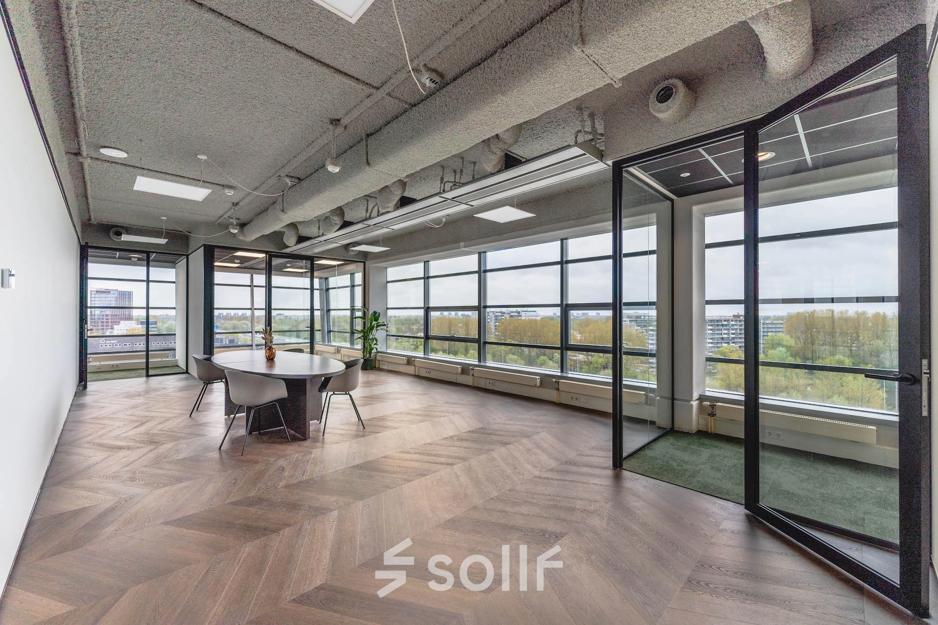 Spacious office to rent at Amsterdam Amstel Business Park, featuring large windows with city views, a round meeting table, and modern furnishings.
