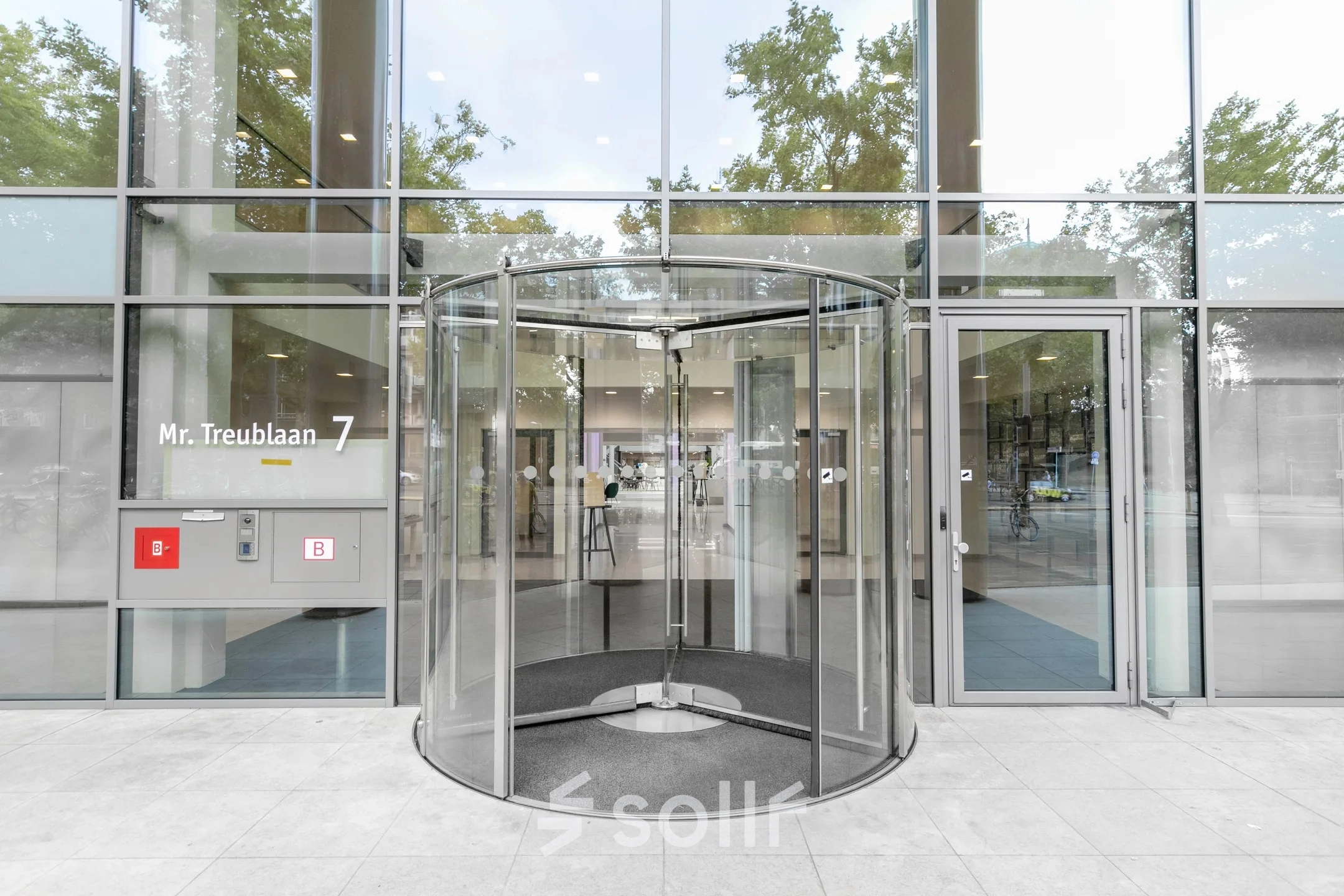 Exterior view of the office building at Mr. Treublaan 7, Amsterdam Amstel, featuring a modern revolving door entrance for office space rental.
