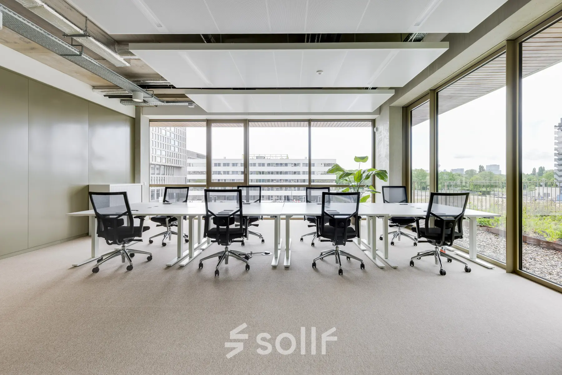 Bright office space with large windows and several desks and chairs, offering a professional workspace for rent in Amsterdam Amstel.