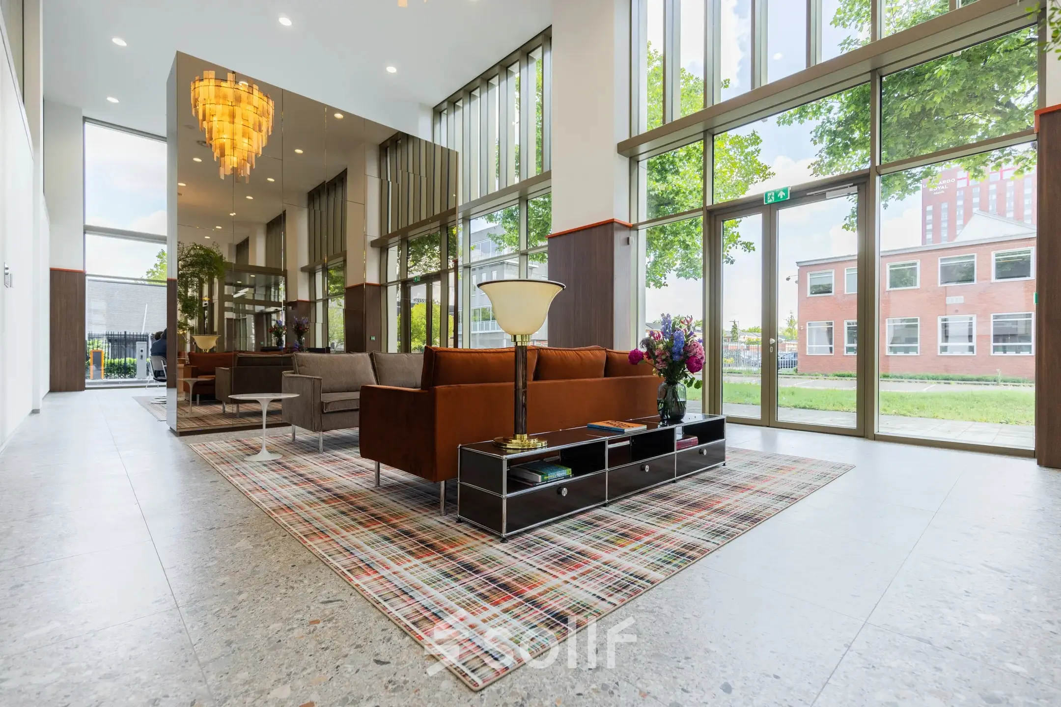 Bright and modern office space with floor-to-ceiling windows, contemporary furnishings, and a stylish chandelier, located at Willem Fenengastraat 16 in Amsterdam Amstel. Ideal for office space rental.
