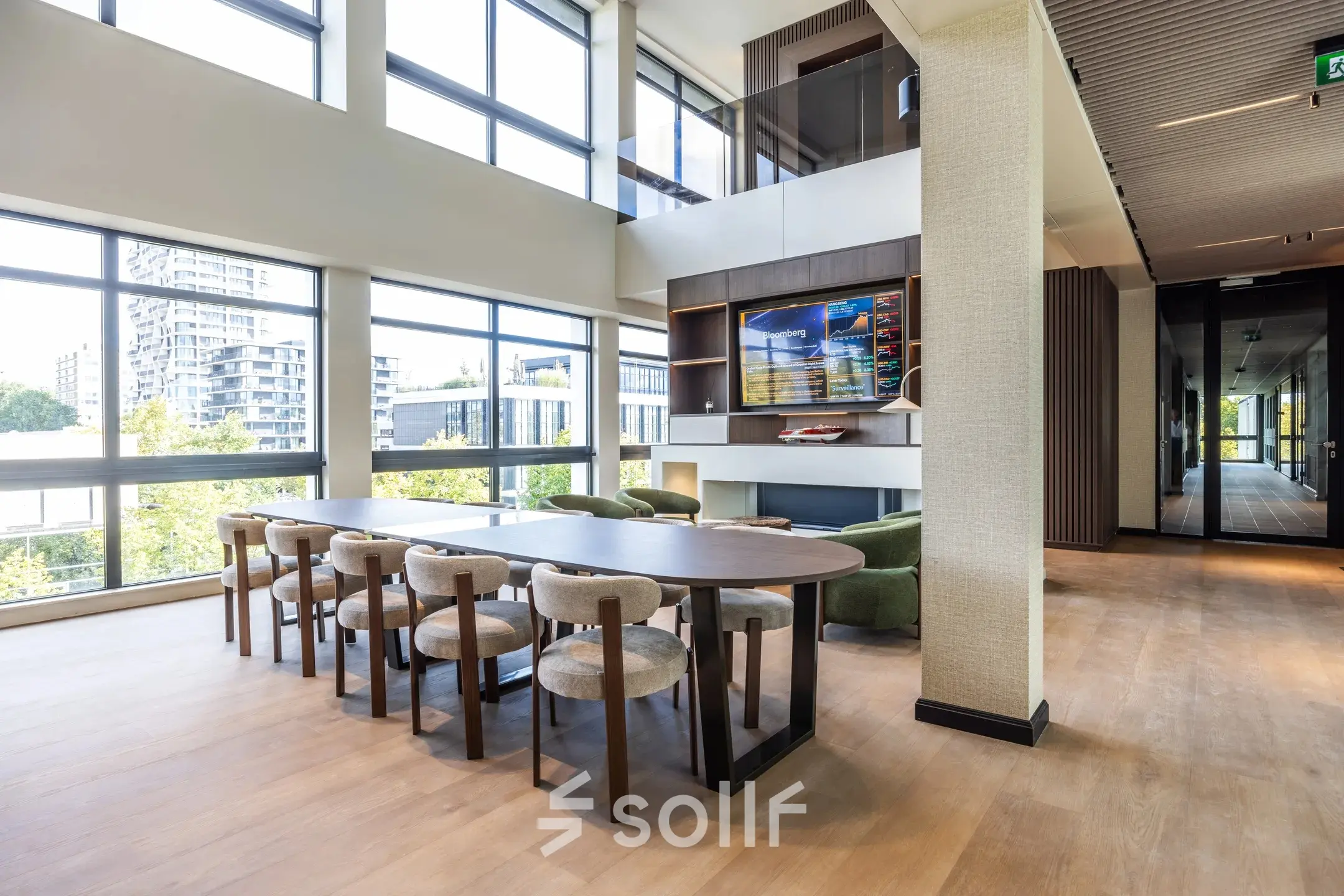 Bright workspace in Amsterdam Buitenveldert featuring a large table with chairs, overlooking an urban view through floor-to-ceiling windows, ideal for office space rental.
