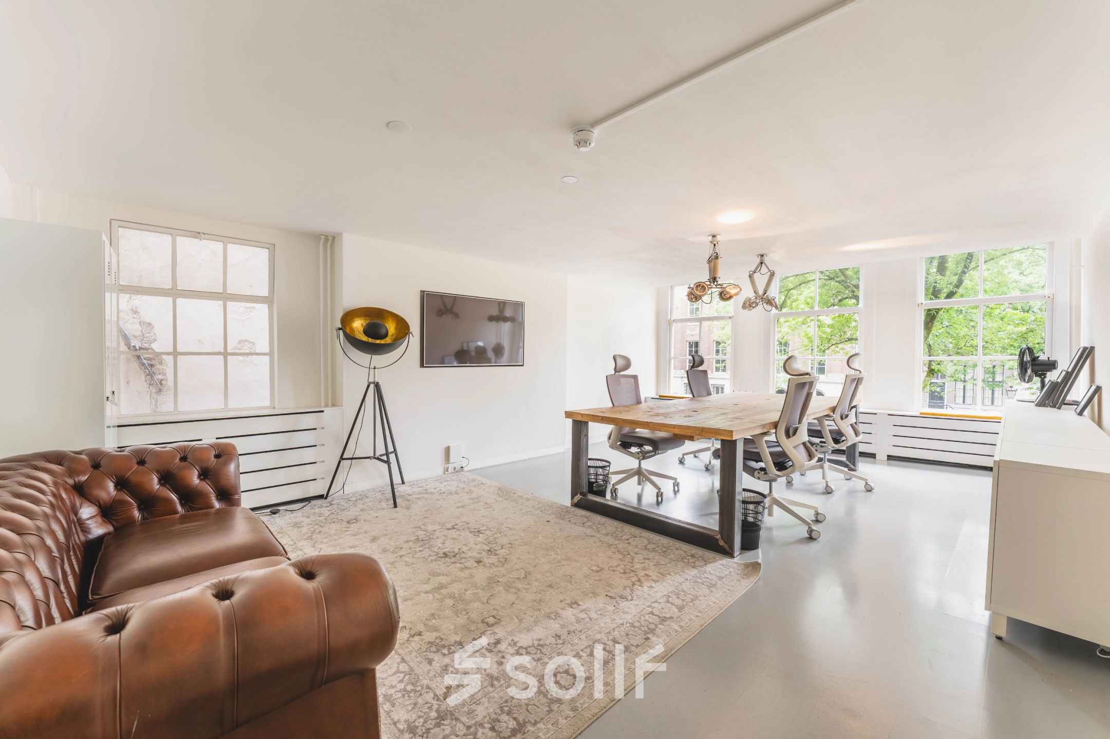 Bright office space for rent at Herengracht 221, Amsterdam Canal Belt, with modern furnishings, including a large wooden table and chairs, facing large windows.