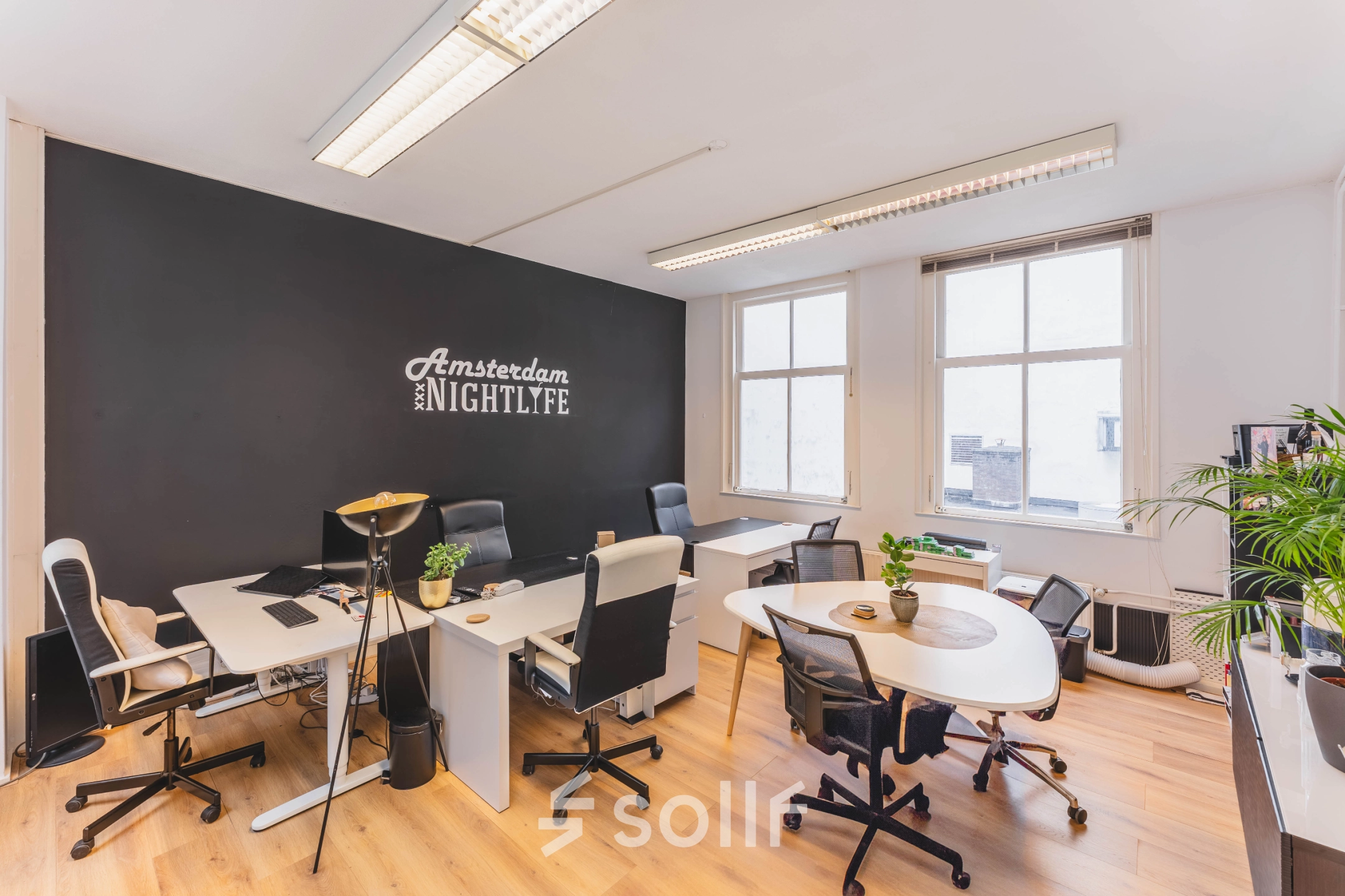 Bright, furnished office space for rent at Herengracht 221, Amsterdam Canal Belt, featuring modern desks and chairs with natural light from large windows.