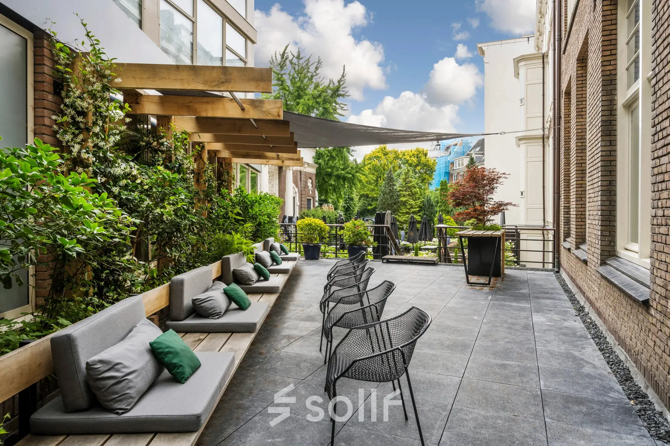 Outdoor seating area at Herengracht 459-469, ideal for office space rental with a mix of comfortable benches and modern chairs amid lush greenery.
