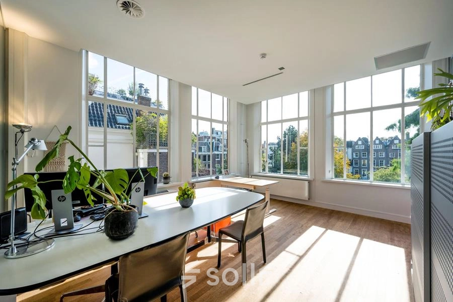 Bright office space rental in Amsterdam Canal Belt at Herengracht 582-584 with large windows, plants, and modern furniture.