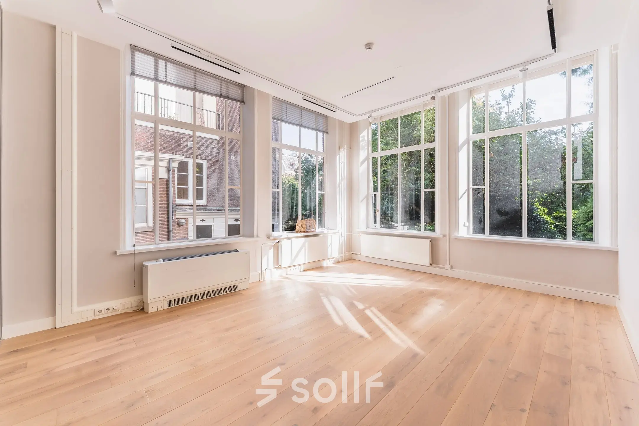 Bright, unfurnished office space available for rent at Herengracht 582-584 in Amsterdam Canal Belt, featuring large windows with garden views and wooden flooring.